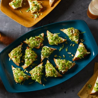 Top view of triangular toasts topped with ricotta cheese and shredded Brussels sprouts on a blue serving platter.