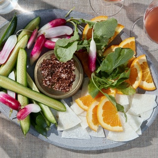 Plate of sliced cucumbers radishes jicama and oranges with a bowl of chili lime salt.