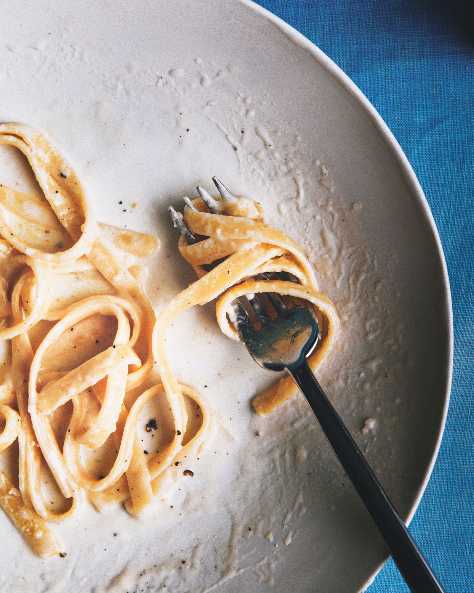 Fettuccini Alfredo in a large shallow serving bowl topped with black pepper and Parmesan.