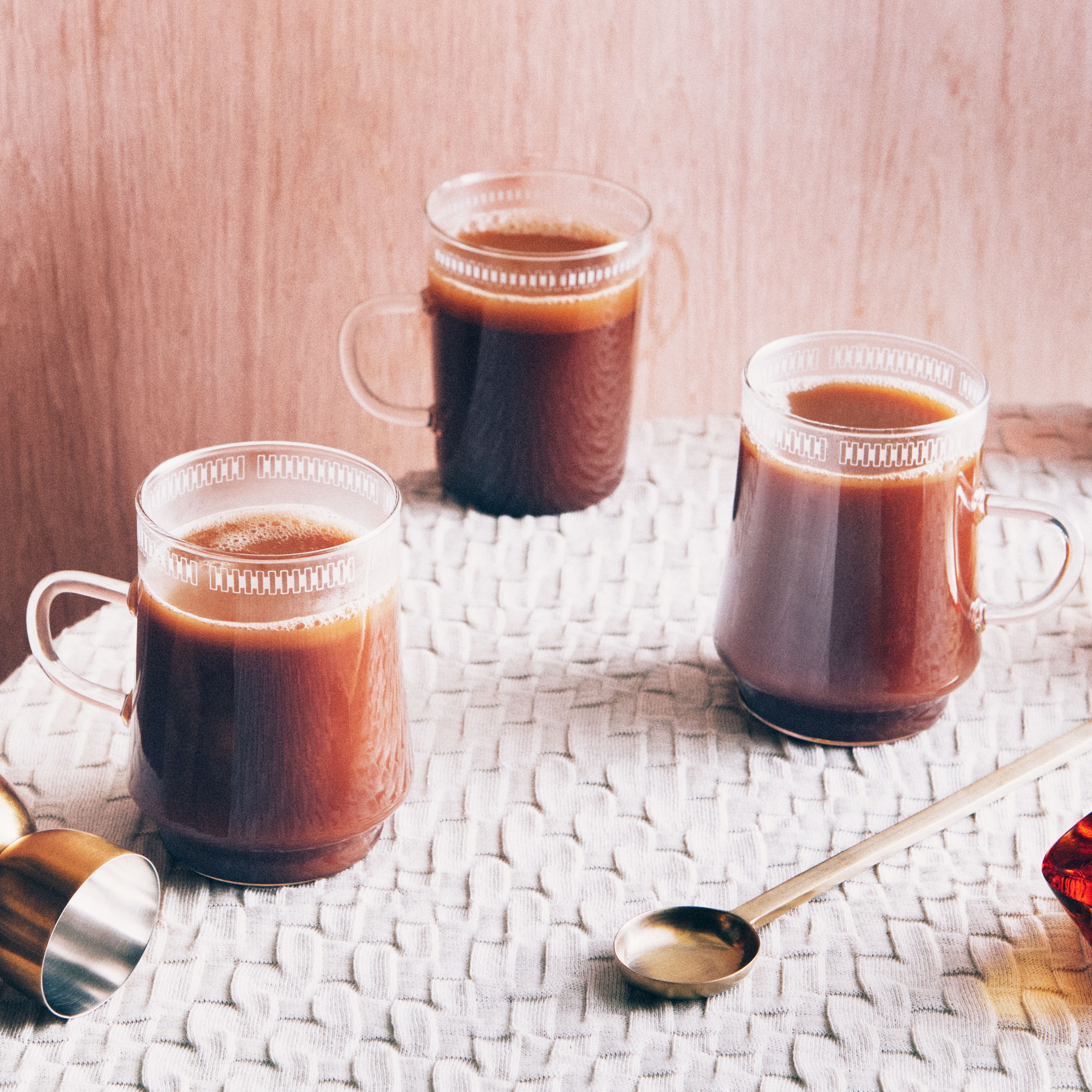 Three hot buttered rum cocktails in glass mugs on a table.