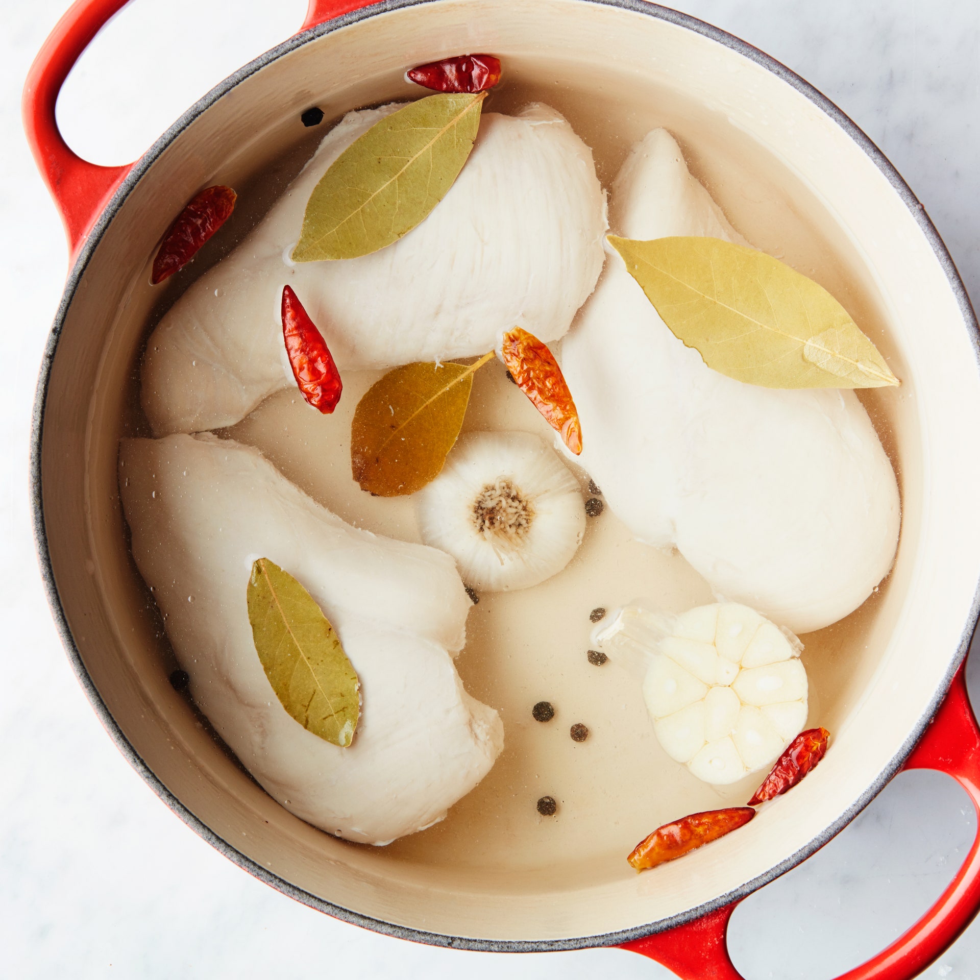 Poached chicken breasts in a dutch oven with bay leaves bird's eye chilies a halved head of garlic and whole black...