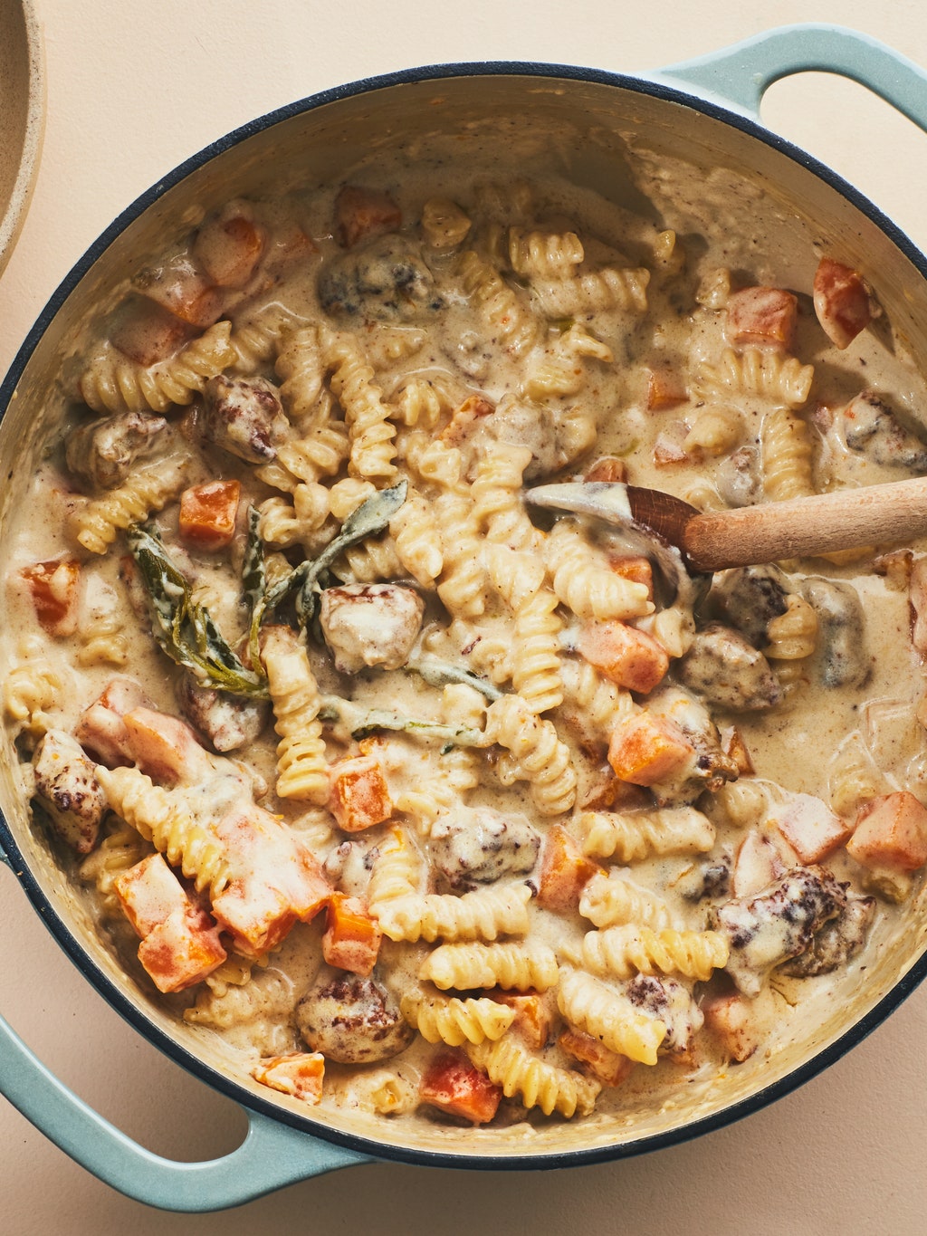 An overhead shot of creamy onepot pasta with sausage and squash with a wooden spoon in the pot.